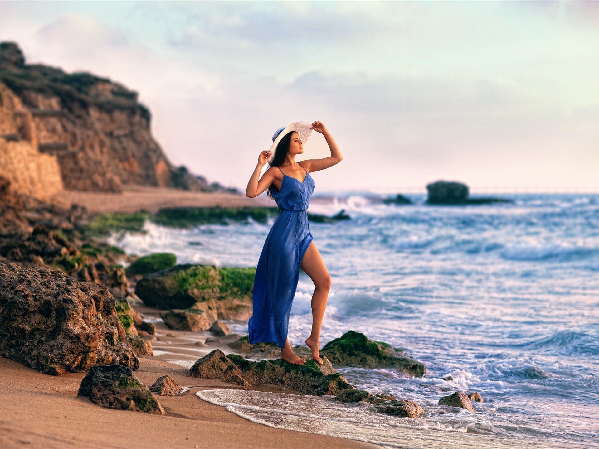 Обнаженная девица с голубыми бусами и парео стоит на берегу моря