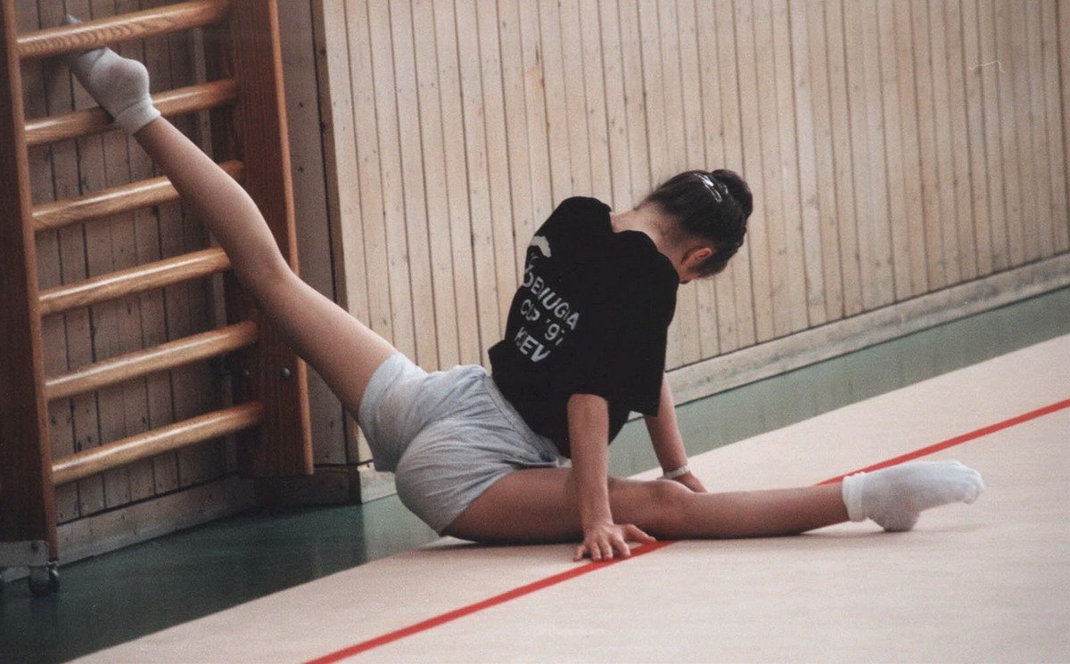 Стройная гимнастка в красном боди делает растяжку в зале на полу