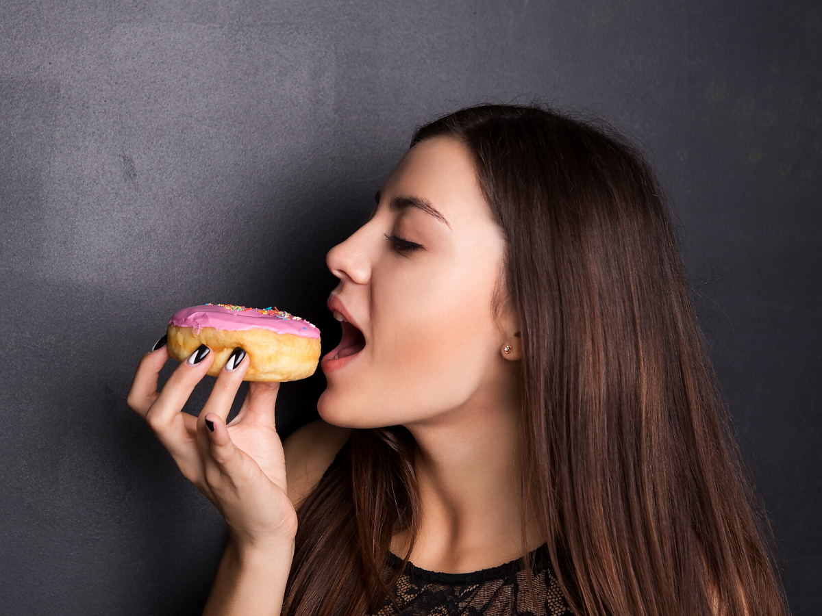 Держит еду во рту. Девушка с пончиком. Девушка ест пончик. Человек ест пончик.